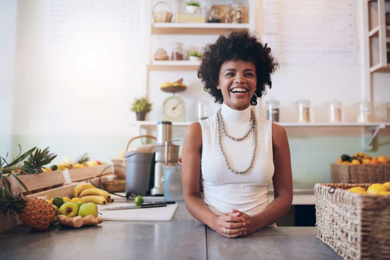 Portrait of young african woman standing behind juice bar counter looking at camera and smiling. Happy juice bar owner.