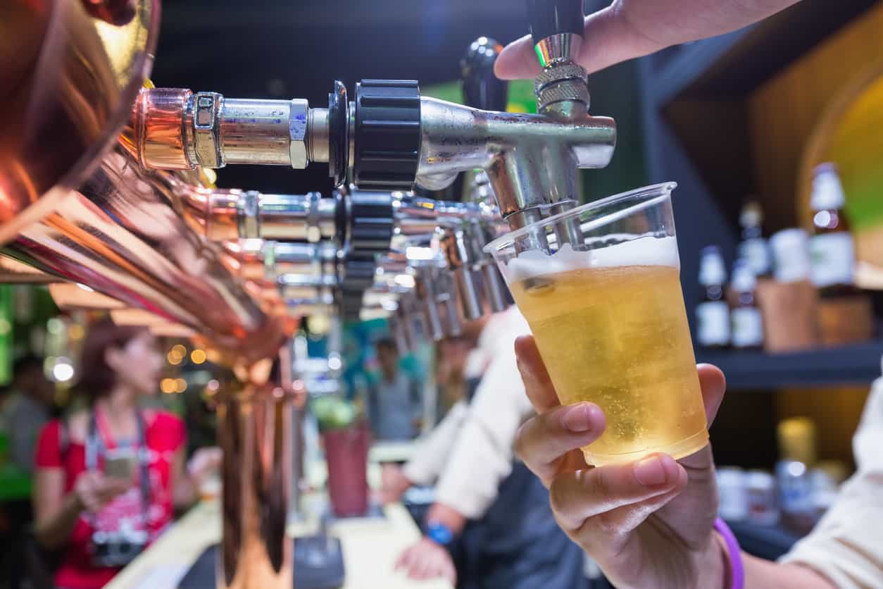 Bartender pouring beer in to a plastic glass with a counter bar background.