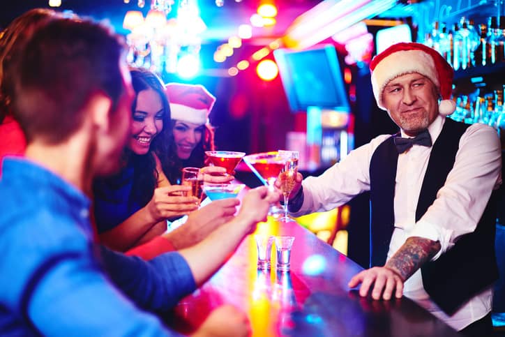 Happy company cheering up by counter with barman in Santa cap near by